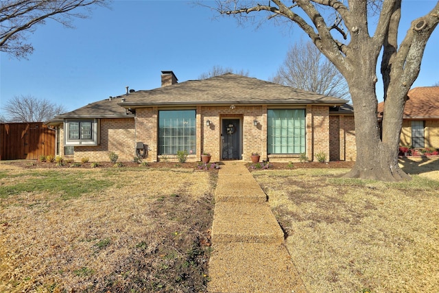 view of front of house with brick siding, a chimney, a front lawn, and fence