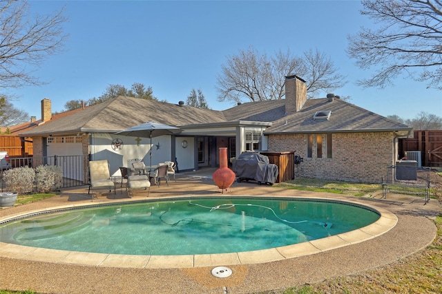 back of house featuring brick siding, a fenced in pool, fence, a chimney, and a patio area