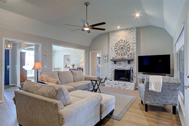 living room with lofted ceiling, a brick fireplace, light wood-style floors, and ceiling fan