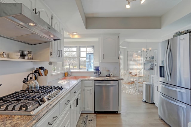 kitchen with ventilation hood, a sink, white cabinets, light wood-style floors, and appliances with stainless steel finishes