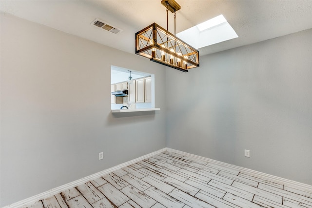 spare room with a chandelier, a skylight, visible vents, and baseboards