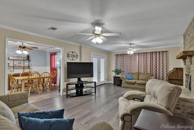 living room with a large fireplace, wood finished floors, visible vents, french doors, and ornamental molding