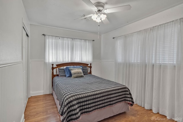 bedroom featuring light wood-type flooring, a ceiling fan, a closet, and wainscoting