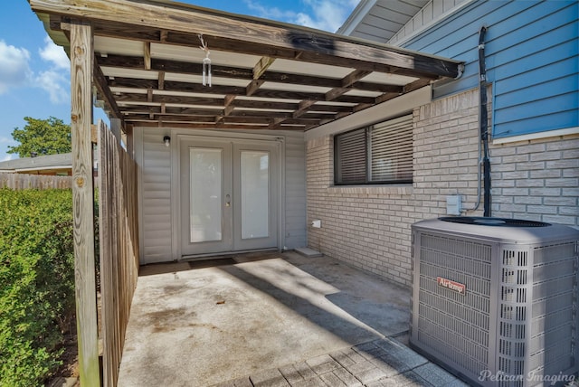 property entrance featuring french doors, brick siding, central AC unit, fence, and a carport