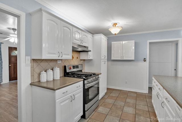 kitchen with stainless steel gas range oven, under cabinet range hood, white cabinetry, decorative backsplash, and dark countertops