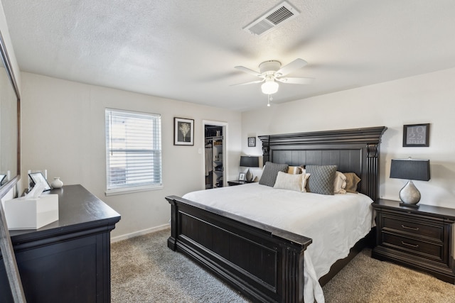 bedroom with visible vents, a ceiling fan, light colored carpet, a spacious closet, and a textured ceiling