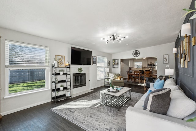 living area with dark wood finished floors, a notable chandelier, a fireplace, a textured ceiling, and baseboards