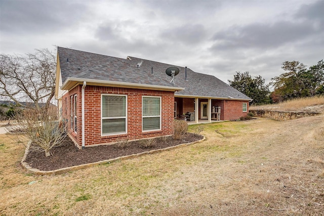 back of property featuring roof with shingles, brick siding, and a lawn