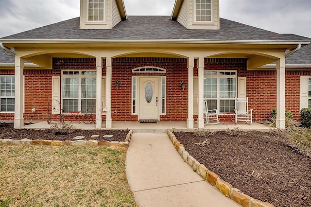 entrance to property with roof with shingles, a porch, and brick siding