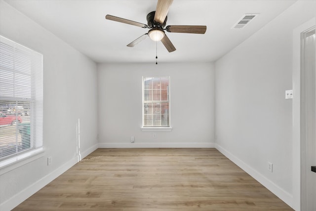 unfurnished room featuring light wood finished floors, plenty of natural light, visible vents, and baseboards