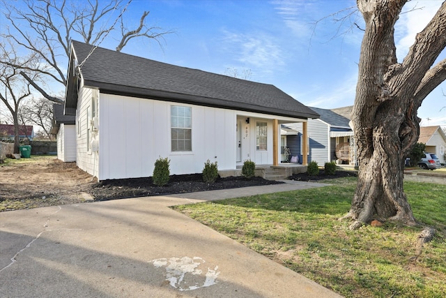 view of front of house with covered porch, a shingled roof, a front lawn, and board and batten siding