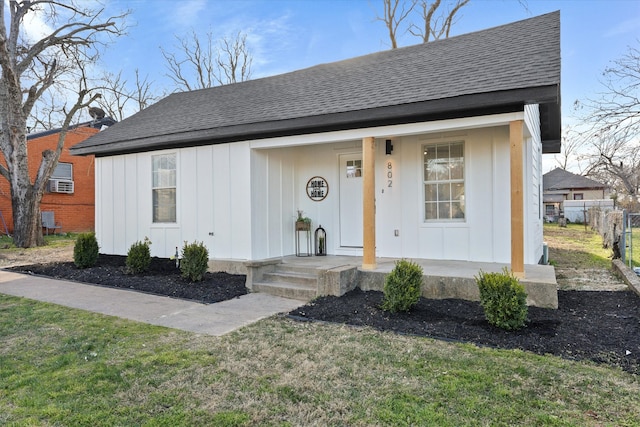 view of front of house with covered porch, roof with shingles, board and batten siding, and fence