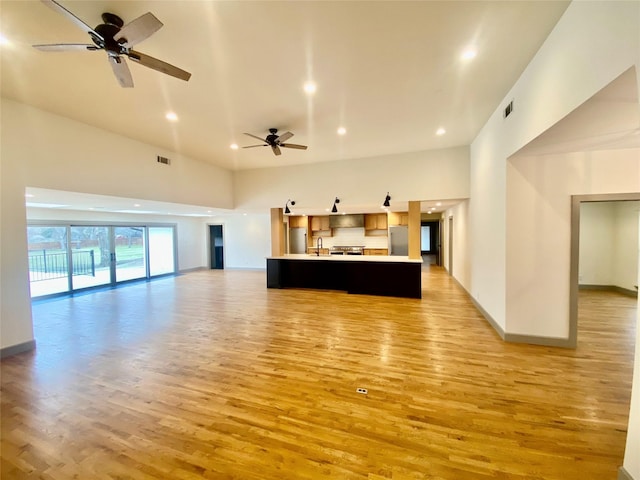 kitchen featuring open floor plan, visible vents, a center island with sink, and light wood finished floors