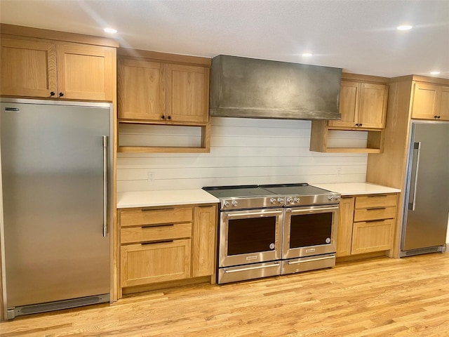 kitchen featuring open shelves, light countertops, light wood-style flooring, appliances with stainless steel finishes, and wall chimney range hood