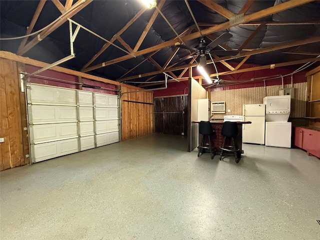 garage featuring wooden walls, stacked washer / dryer, and freestanding refrigerator