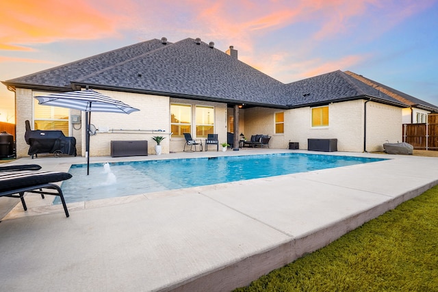 pool at dusk with a patio, fence, and an outdoor pool