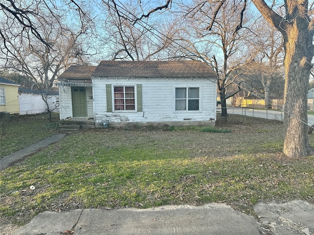 bungalow-style home featuring roof with shingles, fence, and a front lawn