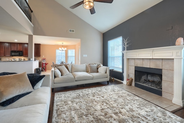 living room featuring a healthy amount of sunlight, visible vents, a tiled fireplace, and ceiling fan with notable chandelier