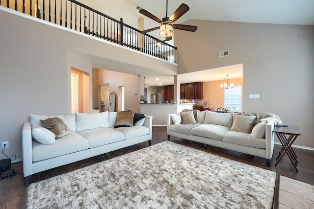 living area with high vaulted ceiling, ceiling fan with notable chandelier, wood finished floors, visible vents, and baseboards