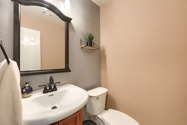 half bathroom with visible vents, a textured wall, vanity, and toilet