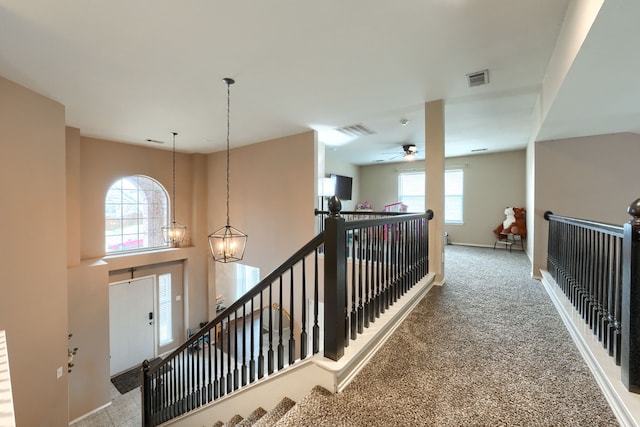 hallway with carpet, visible vents, baseboards, and an upstairs landing