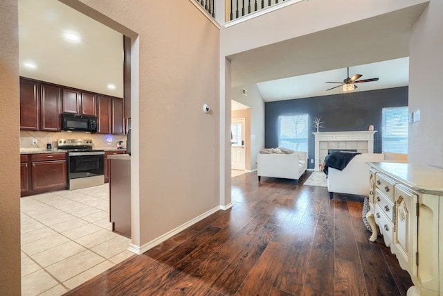 kitchen featuring black microwave, a tile fireplace, electric range, light wood finished floors, and tasteful backsplash