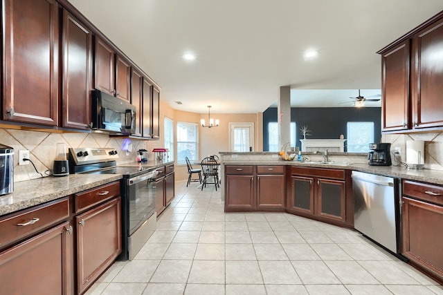 kitchen featuring ceiling fan with notable chandelier, a peninsula, a sink, appliances with stainless steel finishes, and backsplash