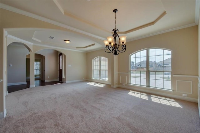 carpeted spare room featuring crown molding, arched walkways, a raised ceiling, and a decorative wall