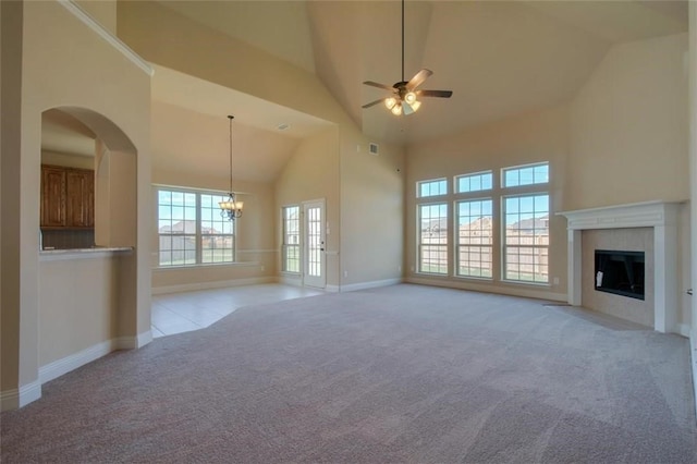 unfurnished living room featuring high vaulted ceiling, a tile fireplace, light colored carpet, ceiling fan with notable chandelier, and baseboards