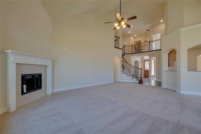 unfurnished living room featuring light carpet, high vaulted ceiling, stairway, and a tile fireplace