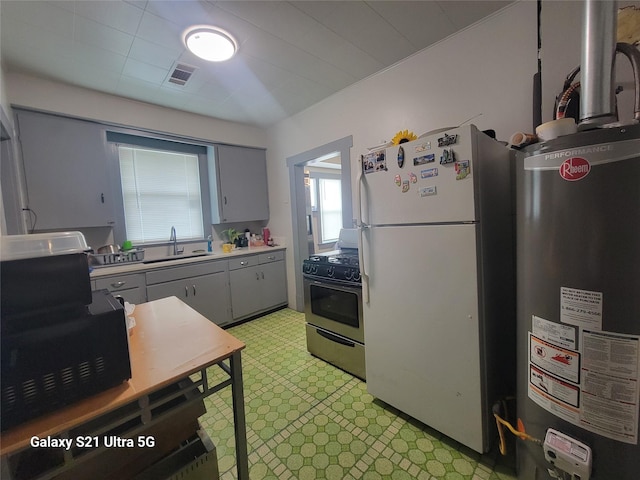 kitchen featuring stainless steel range with gas stovetop, gray cabinetry, a sink, freestanding refrigerator, and light floors