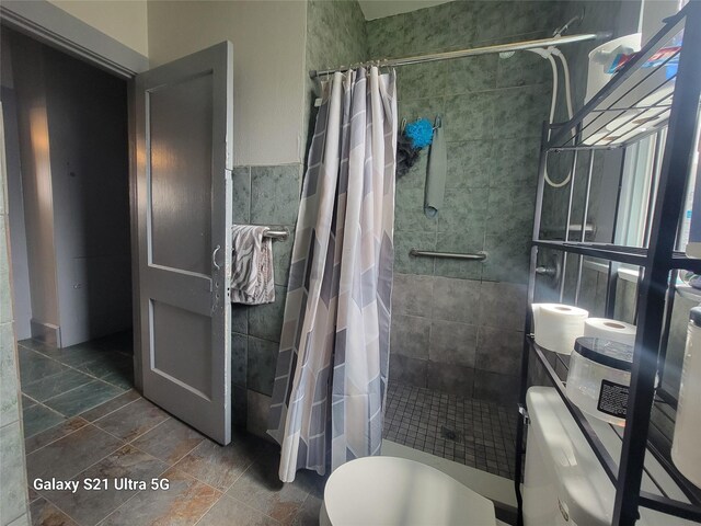 full bath with a tile shower, toilet, and tile walls