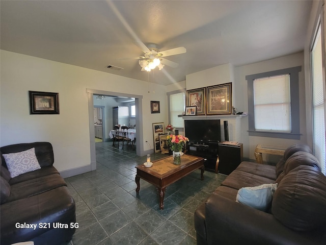 living area with baseboards, visible vents, a wealth of natural light, and a ceiling fan