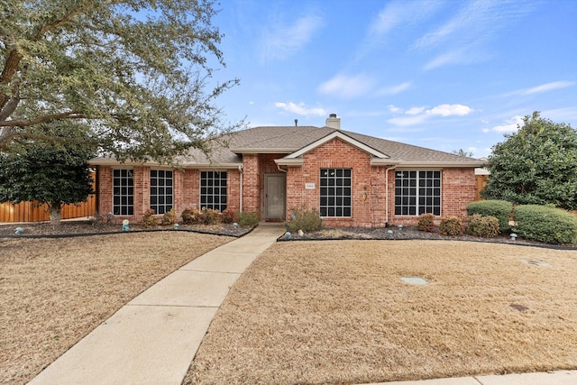 ranch-style home with a shingled roof, brick siding, fence, and a chimney