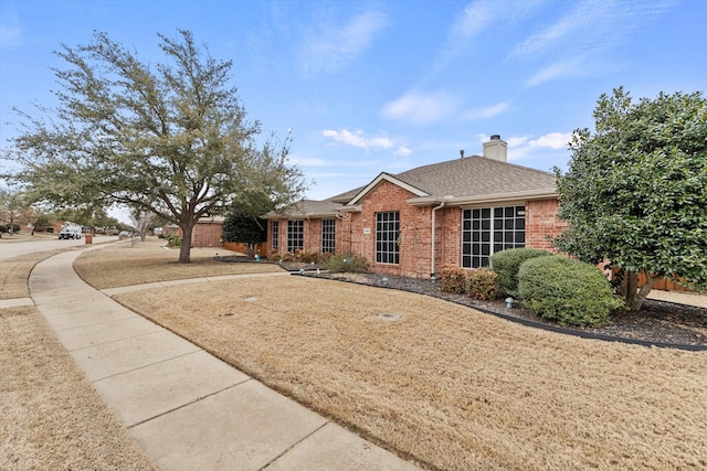 ranch-style house with brick siding, a chimney, and roof with shingles