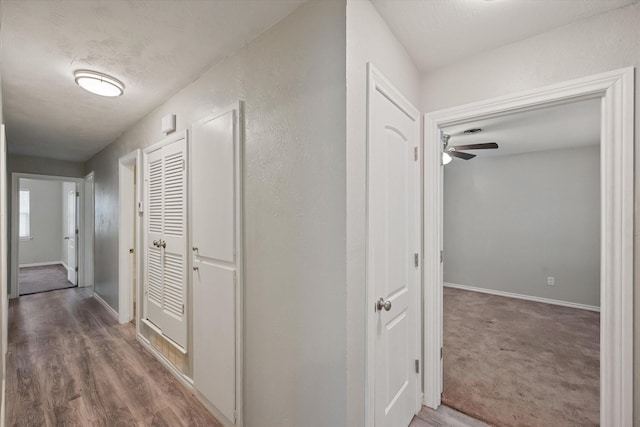 hall featuring carpet, baseboards, and wood finished floors