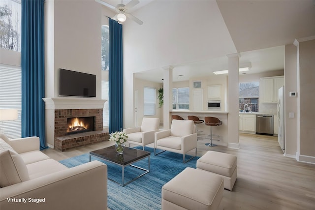 living room with ornate columns, light wood-style flooring, a fireplace, ceiling fan, and a towering ceiling