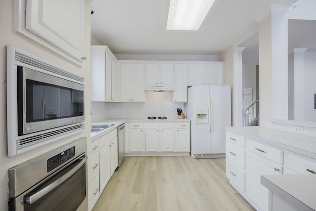 kitchen with tasteful backsplash, under cabinet range hood, light countertops, appliances with stainless steel finishes, and white cabinetry