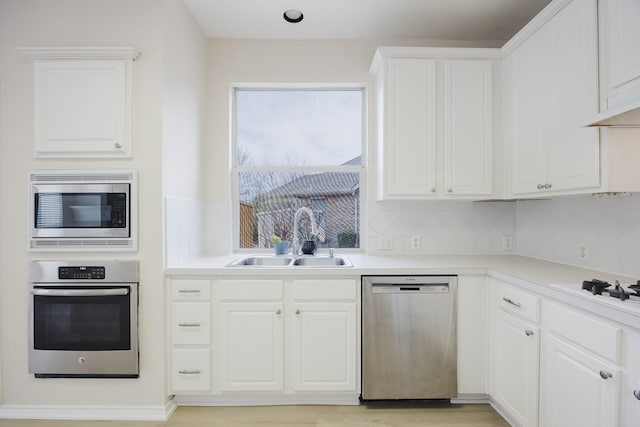 kitchen featuring light wood-style flooring, a sink, stainless steel appliances, white cabinets, and backsplash