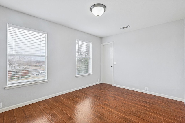 empty room with visible vents, dark wood finished floors, and baseboards