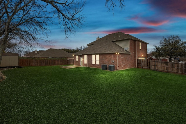 back of house featuring a yard, brick siding, a chimney, and a fenced backyard