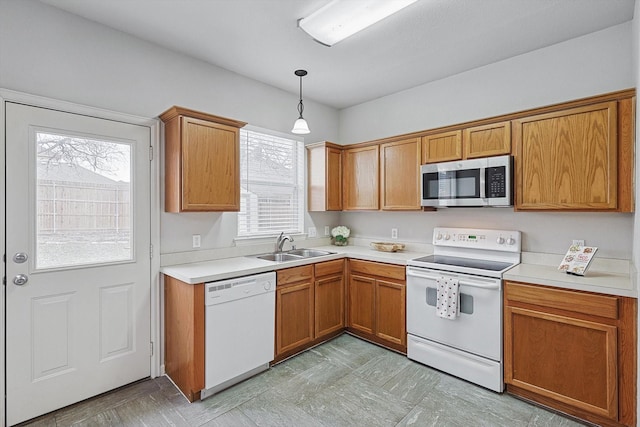 kitchen with white appliances, a sink, light countertops, hanging light fixtures, and brown cabinets