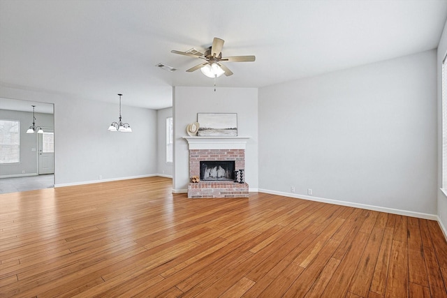 unfurnished living room with a brick fireplace, visible vents, light wood-style floors, and ceiling fan with notable chandelier