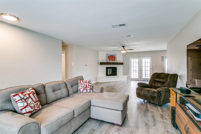 living room with ceiling fan, a brick fireplace, wood finished floors, and visible vents