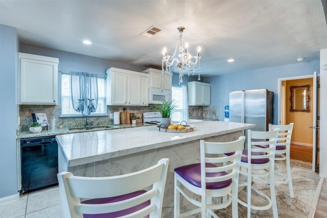 kitchen featuring white appliances, visible vents, a center island, white cabinetry, and pendant lighting