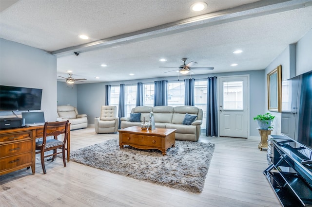 living area with a textured ceiling, a ceiling fan, baseboards, beam ceiling, and light wood finished floors