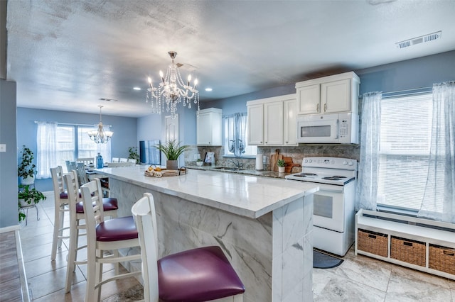 kitchen featuring pendant lighting, white cabinetry, a kitchen island, a chandelier, and white appliances