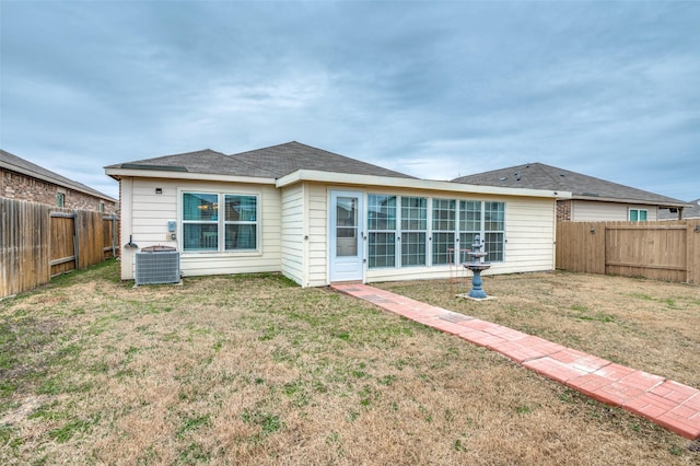 rear view of property featuring central AC, a yard, and a fenced backyard