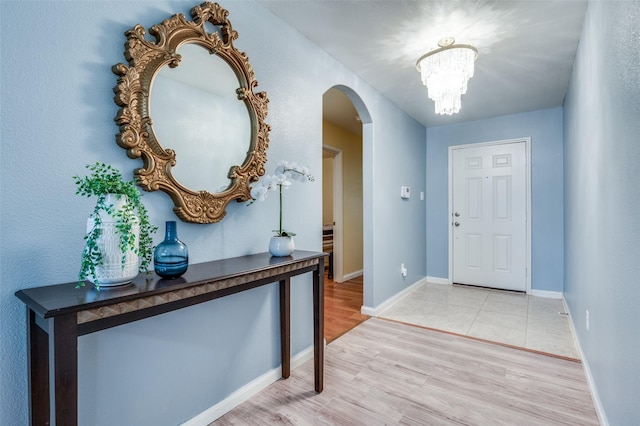 entrance foyer featuring a chandelier, arched walkways, baseboards, and light wood finished floors