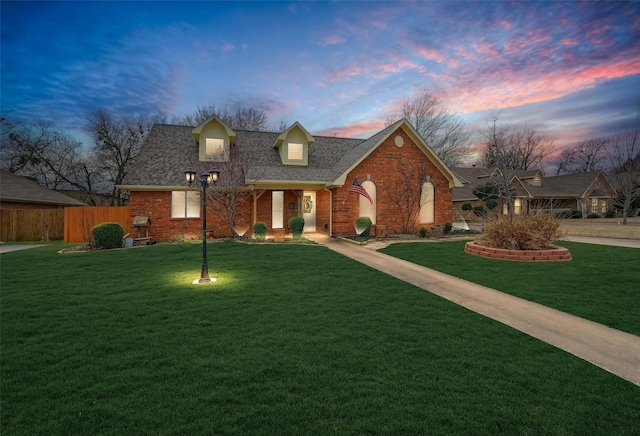 view of front of house with a yard, brick siding, fence, and a shingled roof